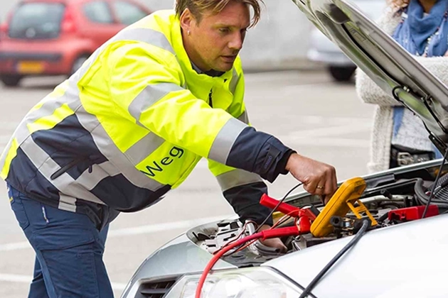 Person in a safety jacket jump-starting a car with open hood.