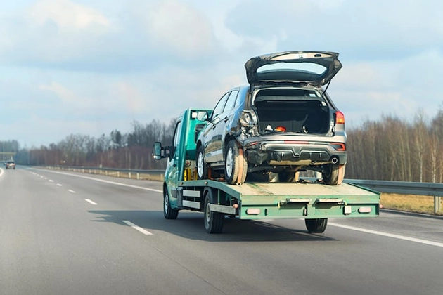 Car being towed on a flatbed truck on a highway.