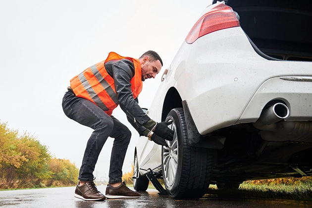 Man changing a flat tire on a white car by the roadside.