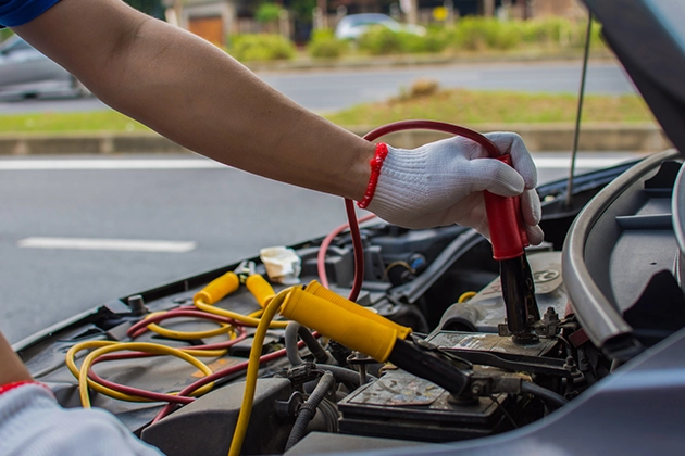 Person using jumper cables on a car battery by the roadside.