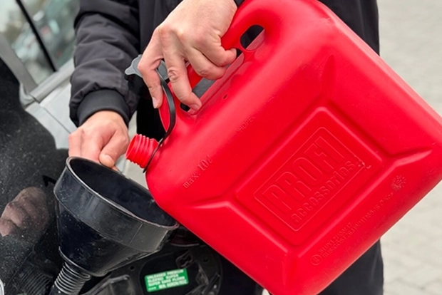 Person pouring gasoline from red container into car using funnel.