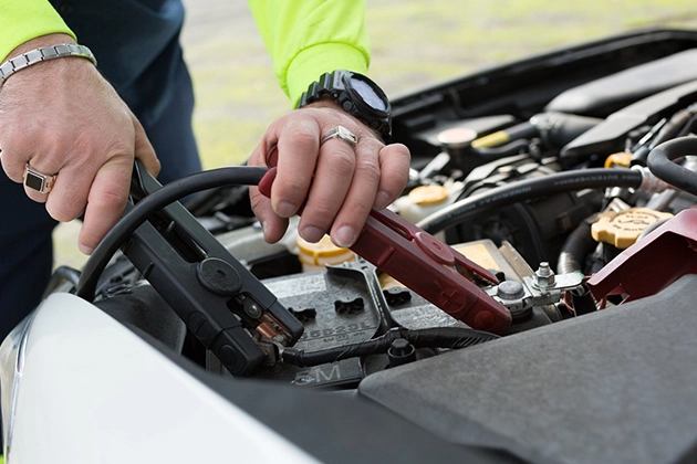 Hands connecting jumper cables to a car battery outdoors.