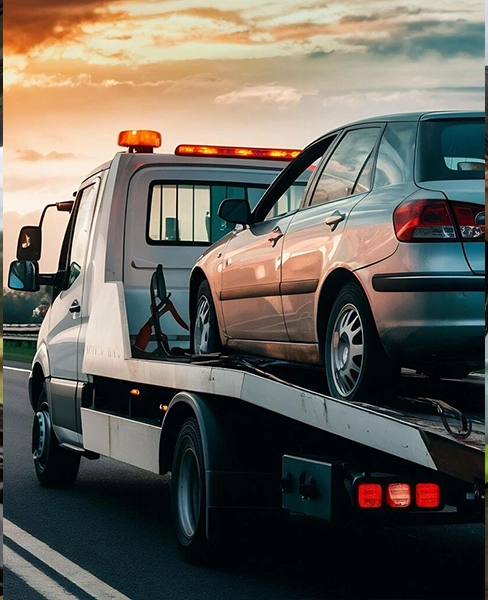 Tow truck transporting a silver car during sunset on a highway.