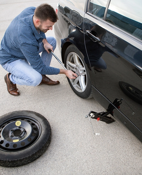 Man changing a car tire with a spare wheel nearby.