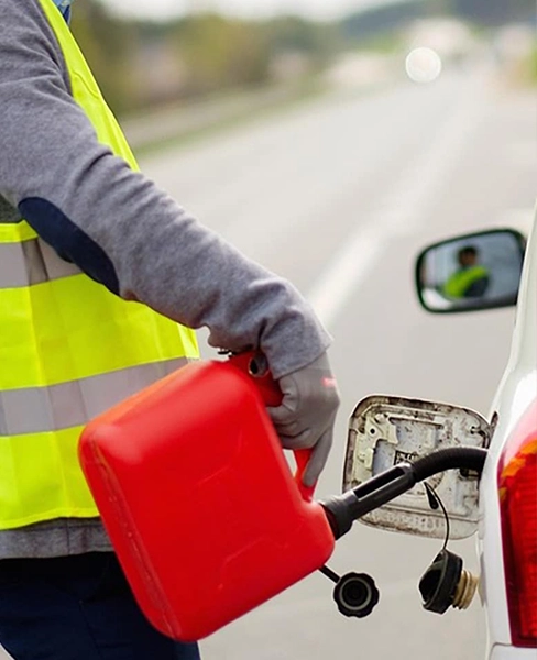 Person refueling car with red gas can on roadside.